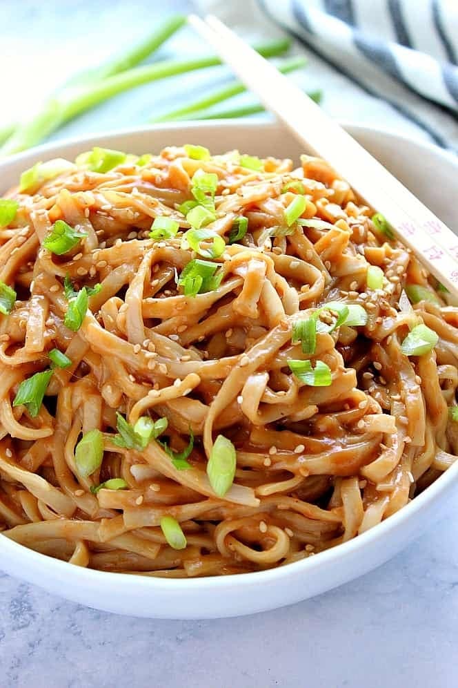 Noodles on a bowl with peanut butter sauce, sesame seeds and chopped onion leaves. 