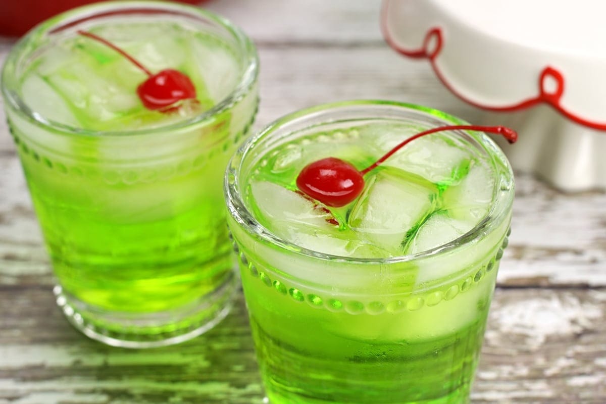 Two glasses of iced green cocktail garnished with cherry.