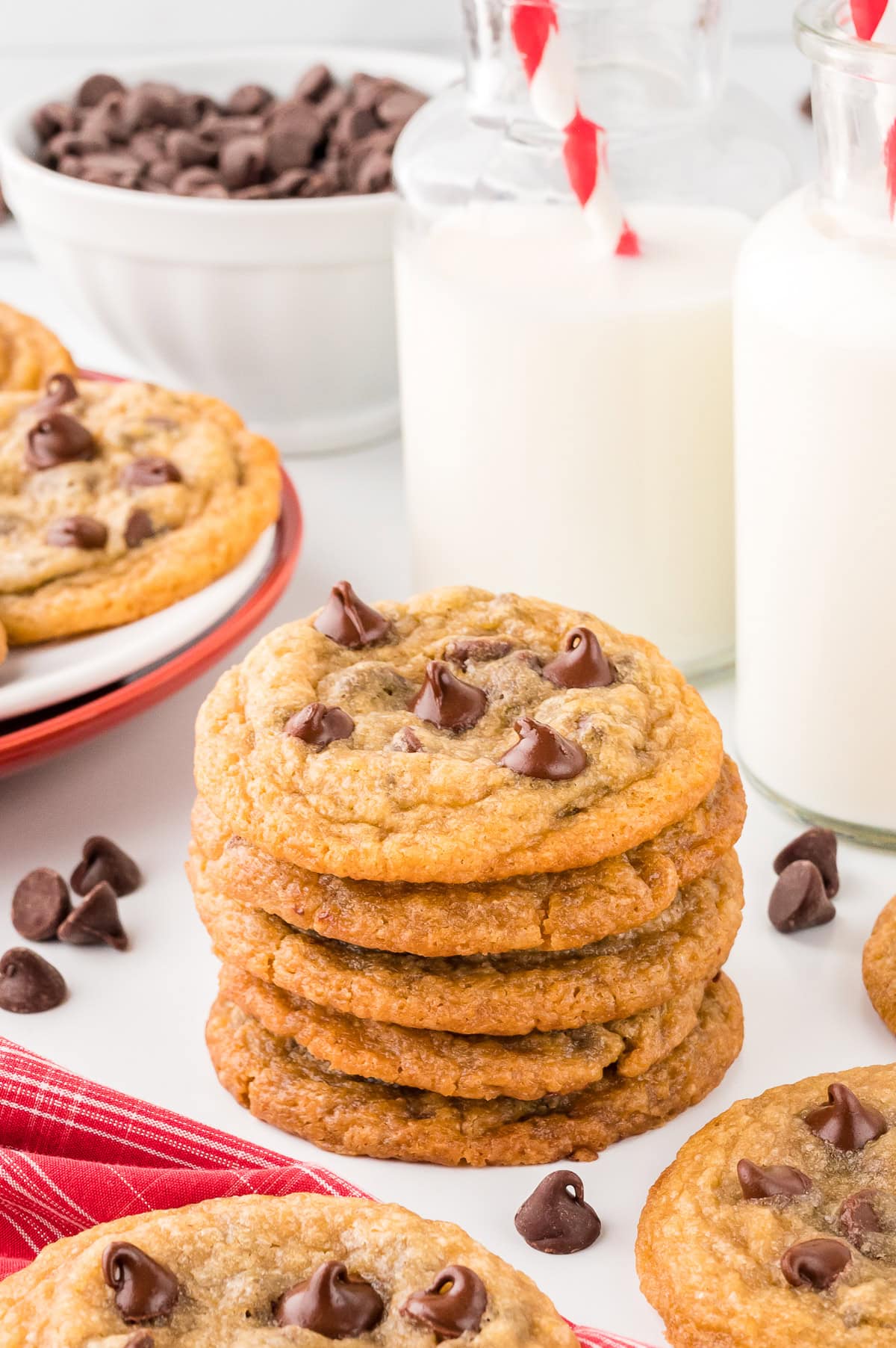 Stack of Toll House Chocolate Chip Cookies on a white table, with milk bottles at the back.