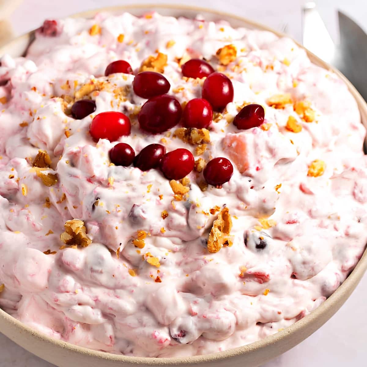 Top view of a bowl of creamy salad with walnuts and cranberries on top.