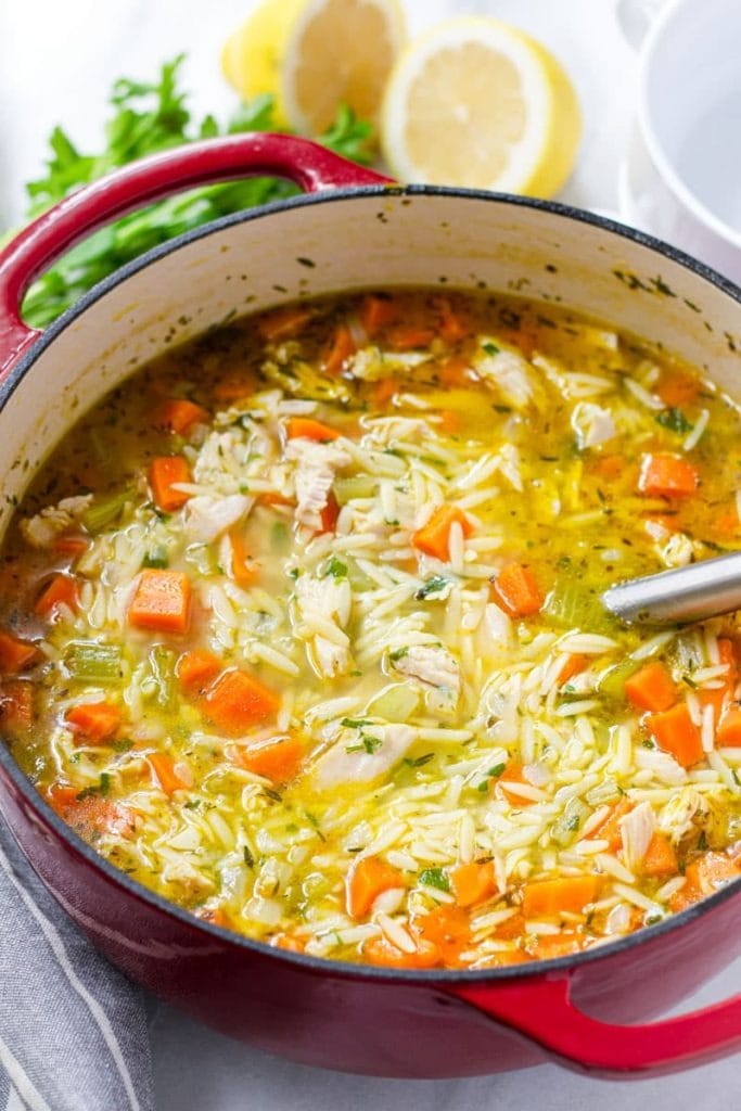 Soup on a red pot with orzo pasta and loaded with carrots and shredded turkey meat. 