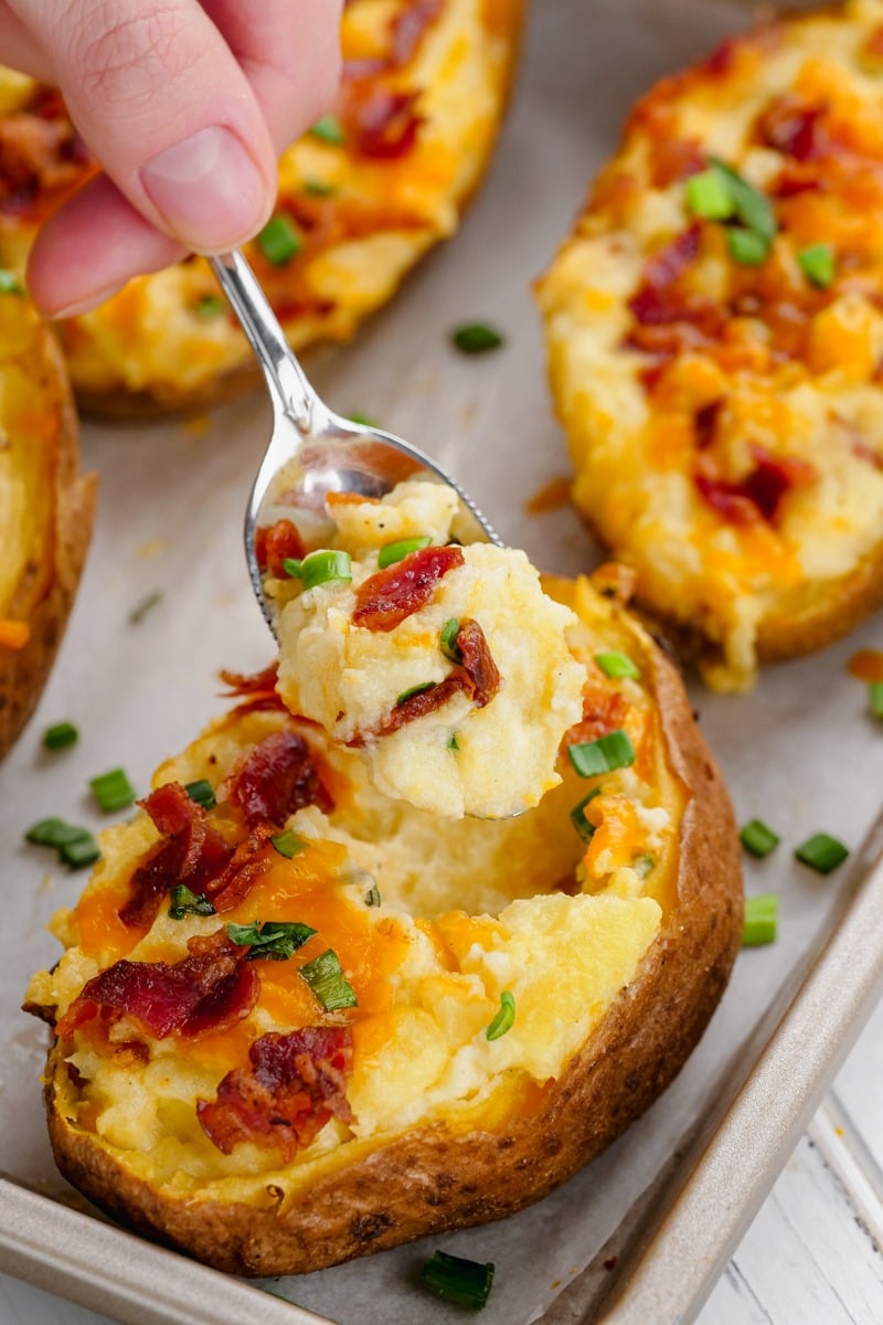 Small spoon scooping cheesy twice baked potatoes served with fried bacon bits and herbs.