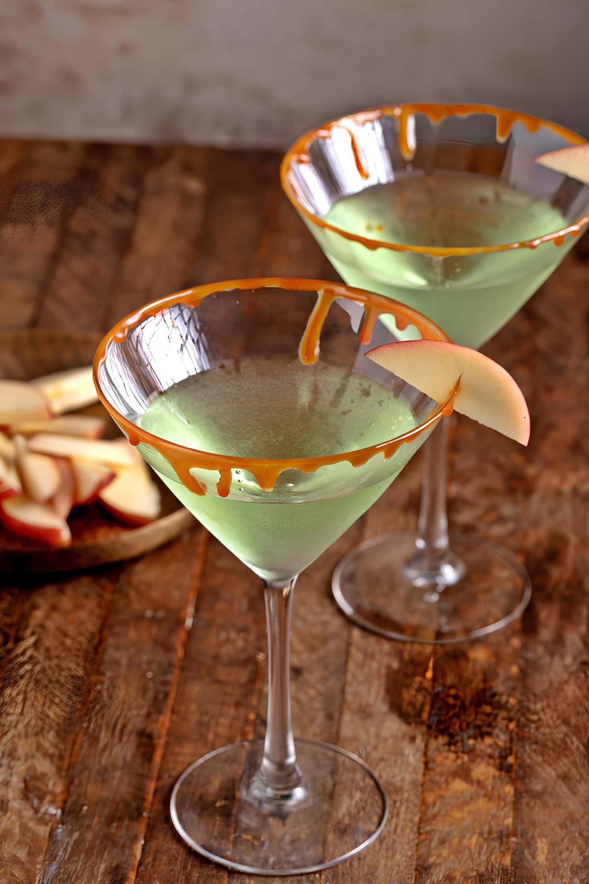 Two martini glasses with caramel and apple on a wooden table