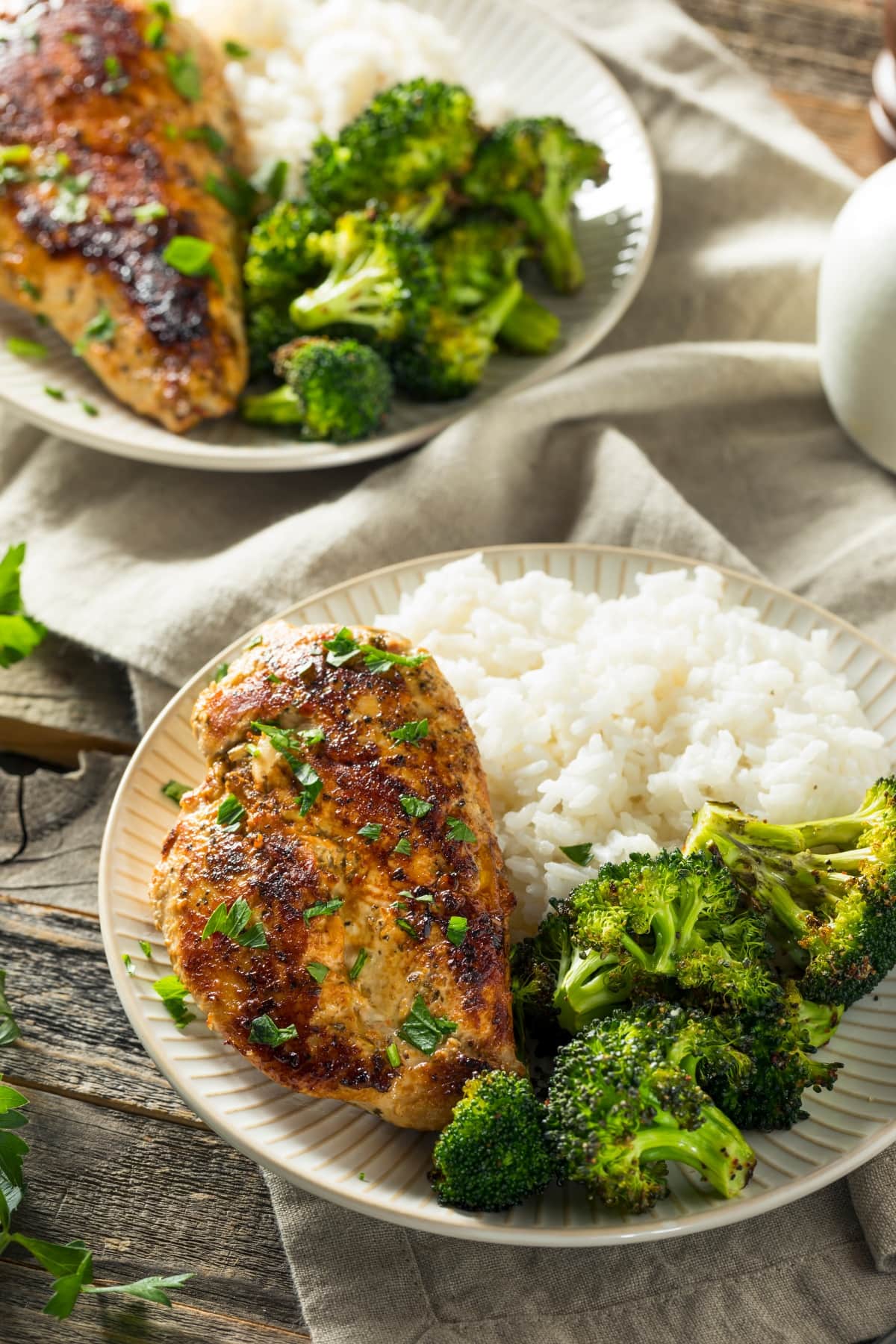Two plates of food with rice, broccoli and baked chicken breast