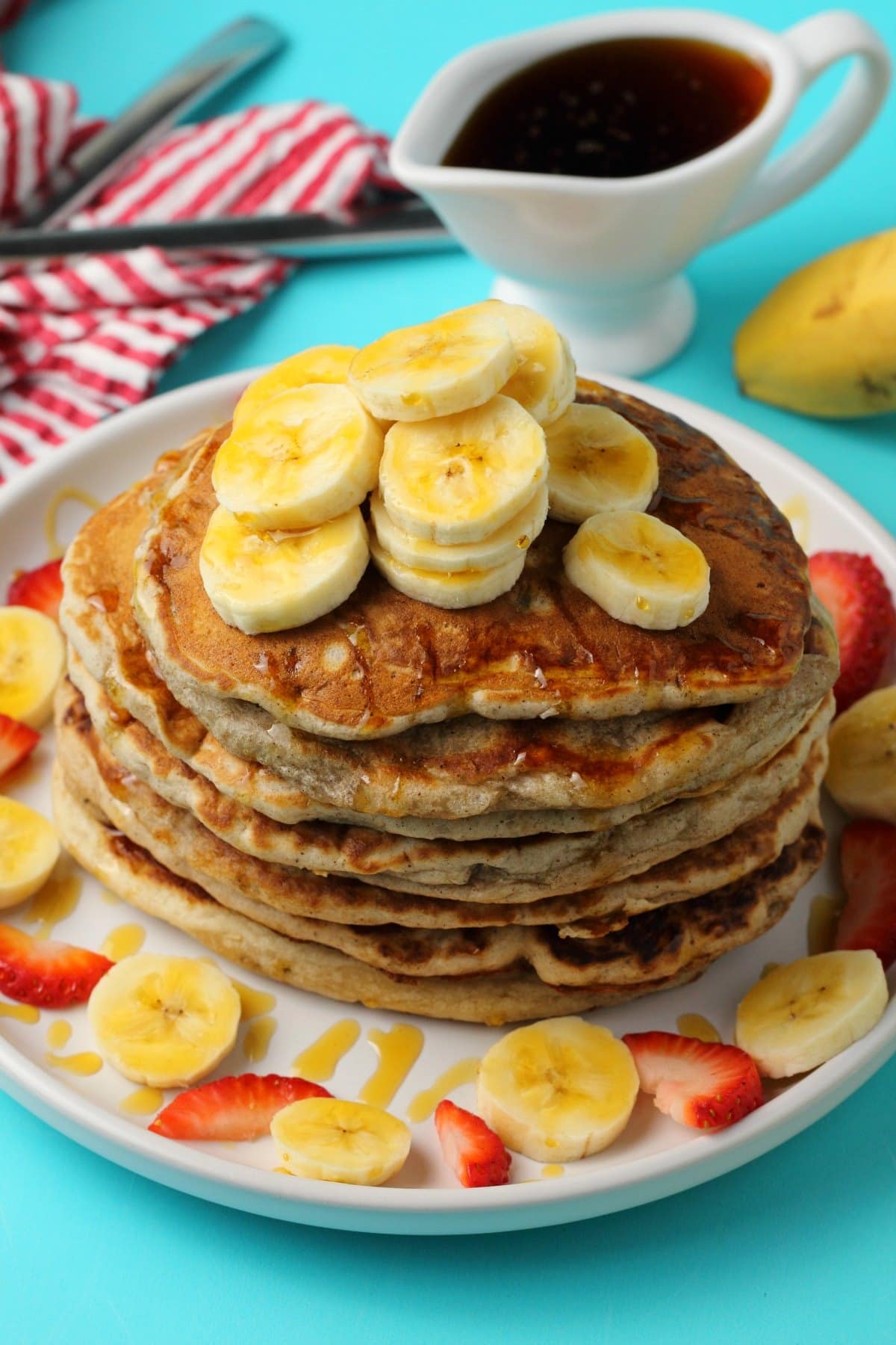 Stack of pancake topped with slices of banana and maple syrup.
