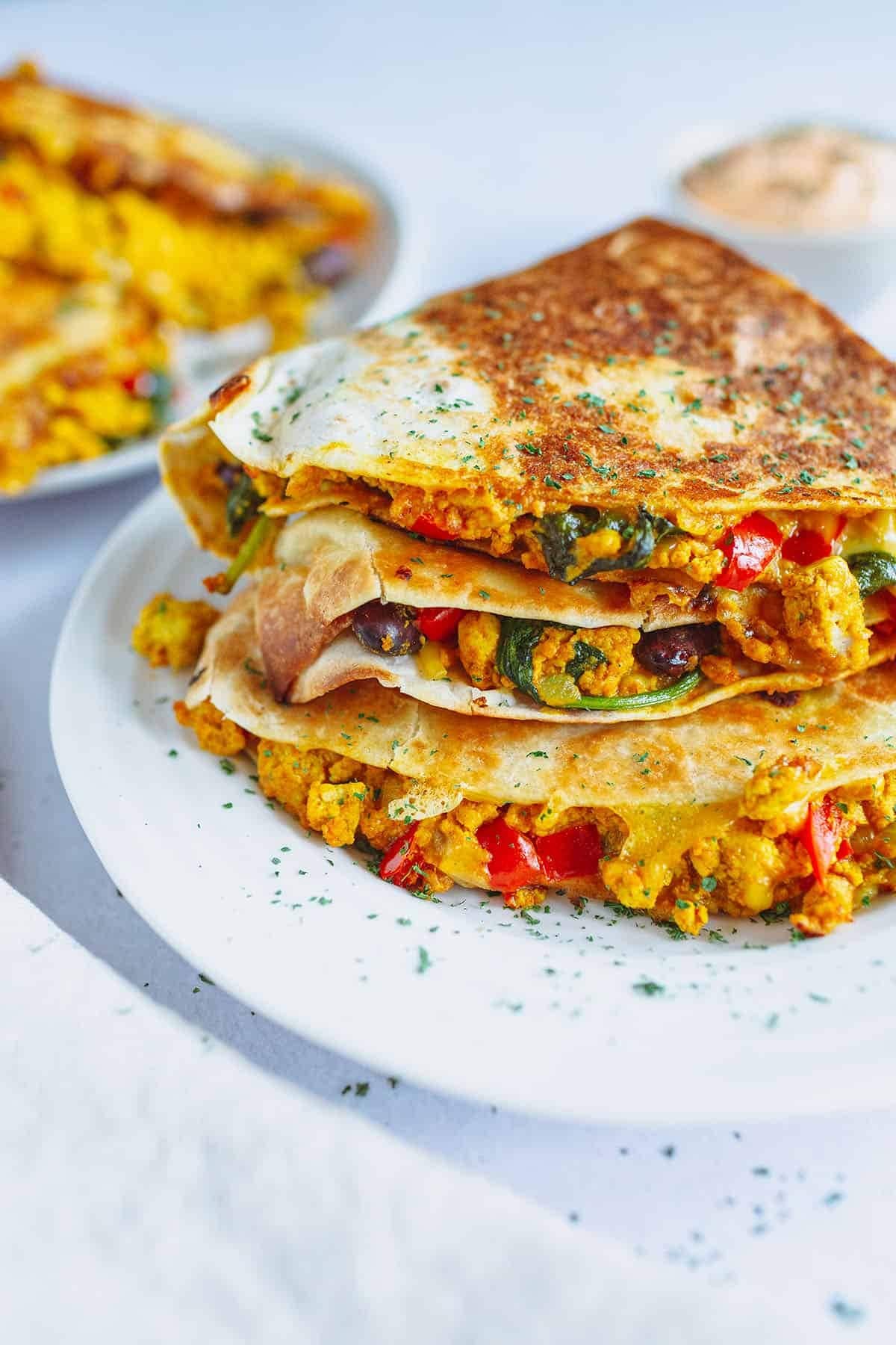 Quesadilla with with a tofu scramble, red peppers, red kidney beans, spinach, and vegan cheese filling.