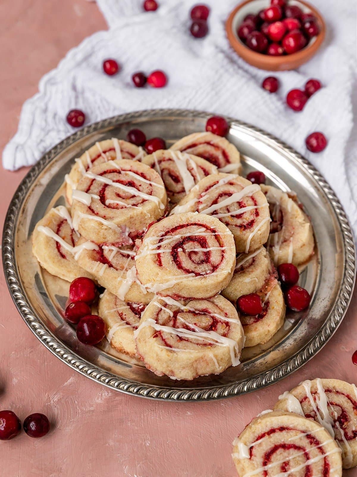 Bunch of pinwheel cookies with cranberry filling on a plate drizzled with white chocolate syrup.