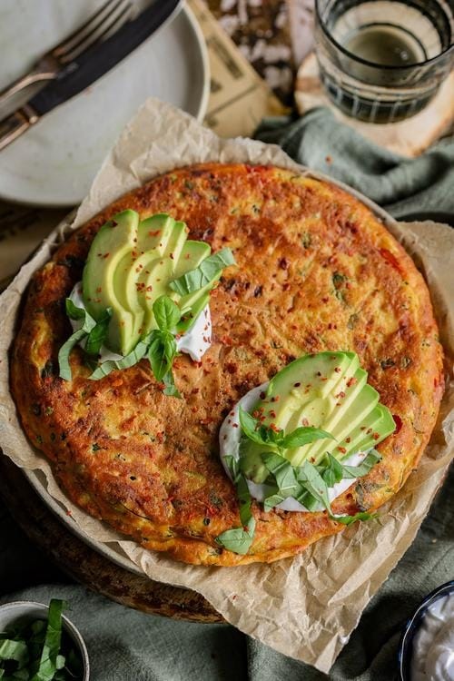 Frittata topped with sliced avocado and basil leaves.