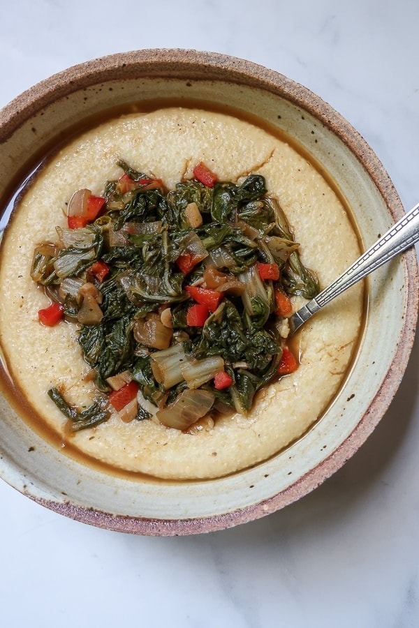 Succulent sauteed greens atop a bed of thick, creamy grits on a bowl. 