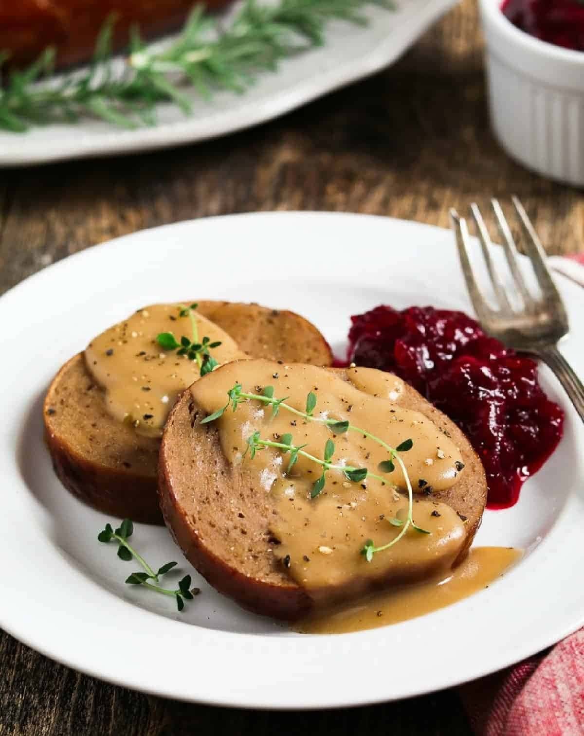 Sliced vegan roast with gravy on top served with cranberry sauce on the side. 