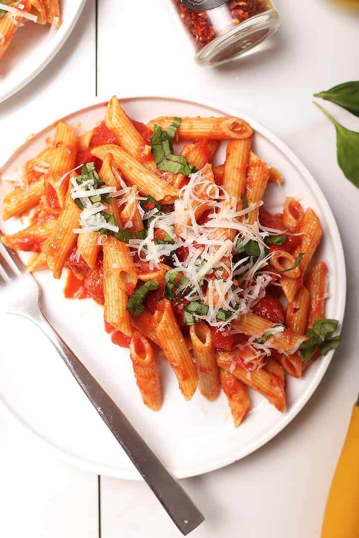 Penne pasta with tomato sauce topped with cheese and chopped parsley leaves. 