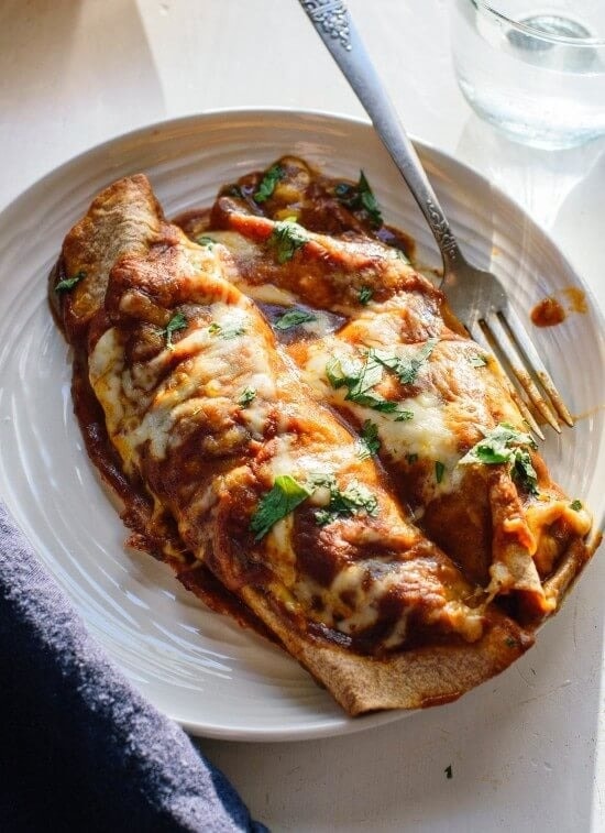 Two pieces of enchiladas topped with chopped parsley served on a plate with fork