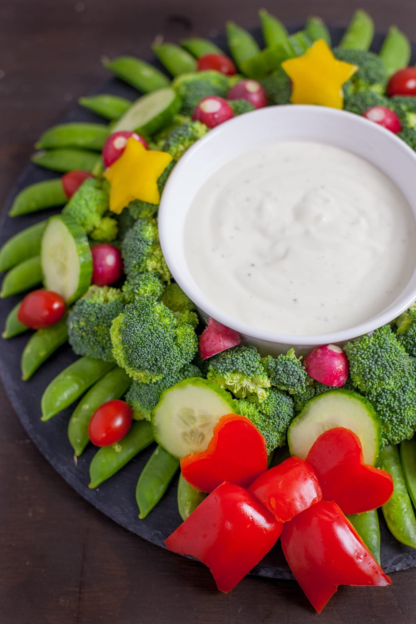 Sliced green veggies arranged with Christmas wreath inspiration served with dipping sauce. 