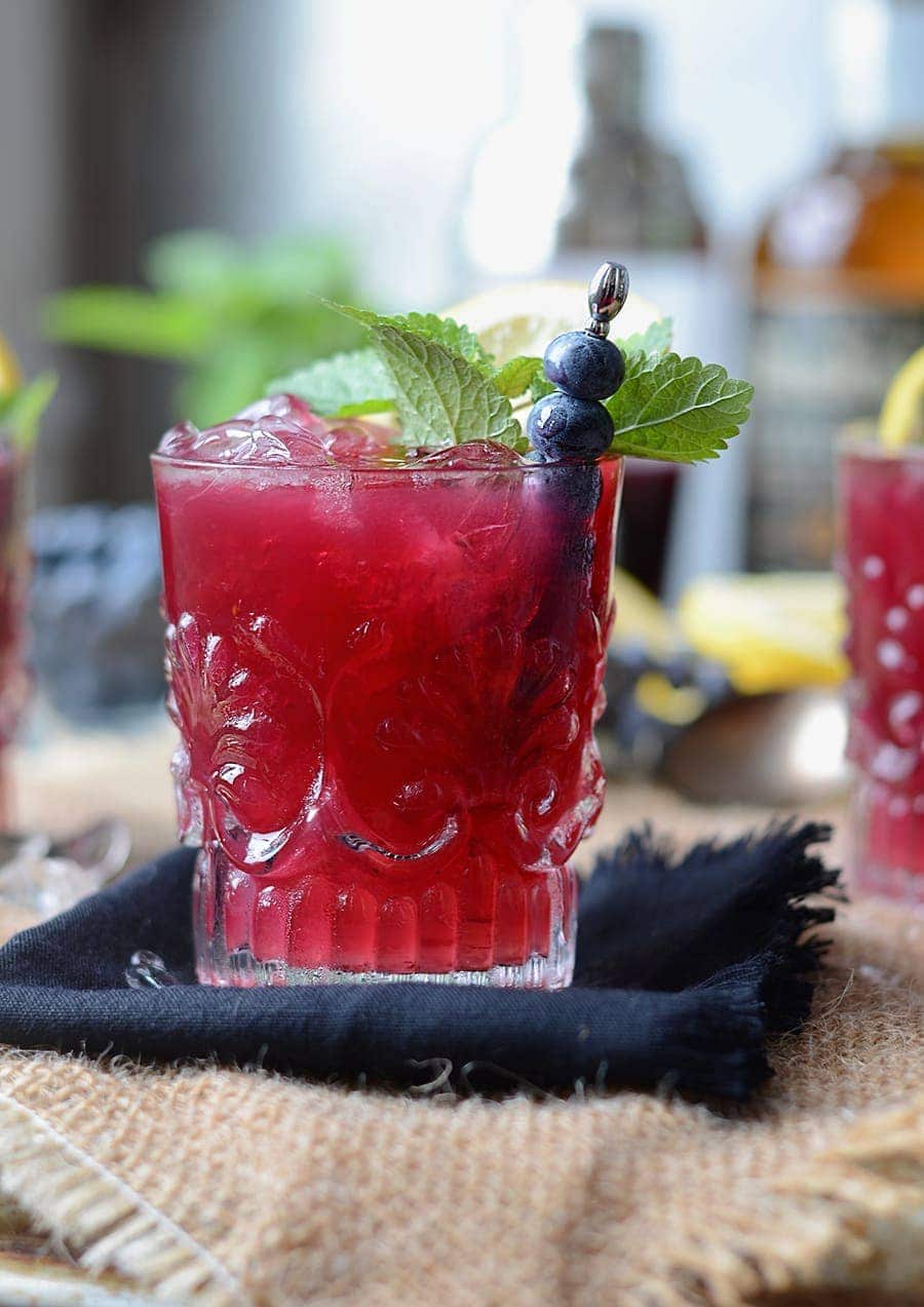 Semi-sweet and semi-bitter blueberry whiskey buck in a decorative glass with blueberries and mint as a garnish