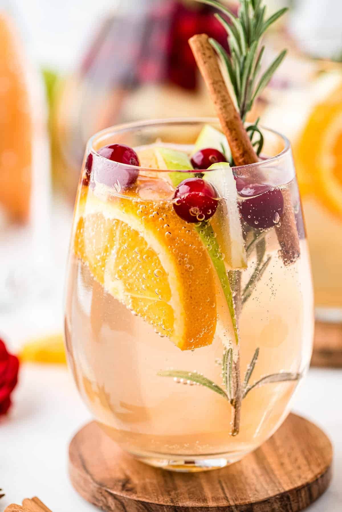 White sangria on a glass garnished with cranberries, orange slices, pears and cinnamon stick.