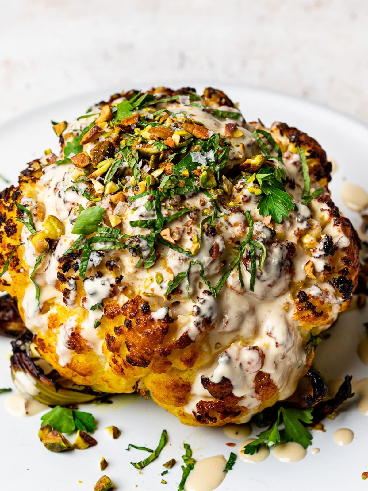 Roasted cauliflower drizzled with white sauce, chopped parsley leaves and seeds.