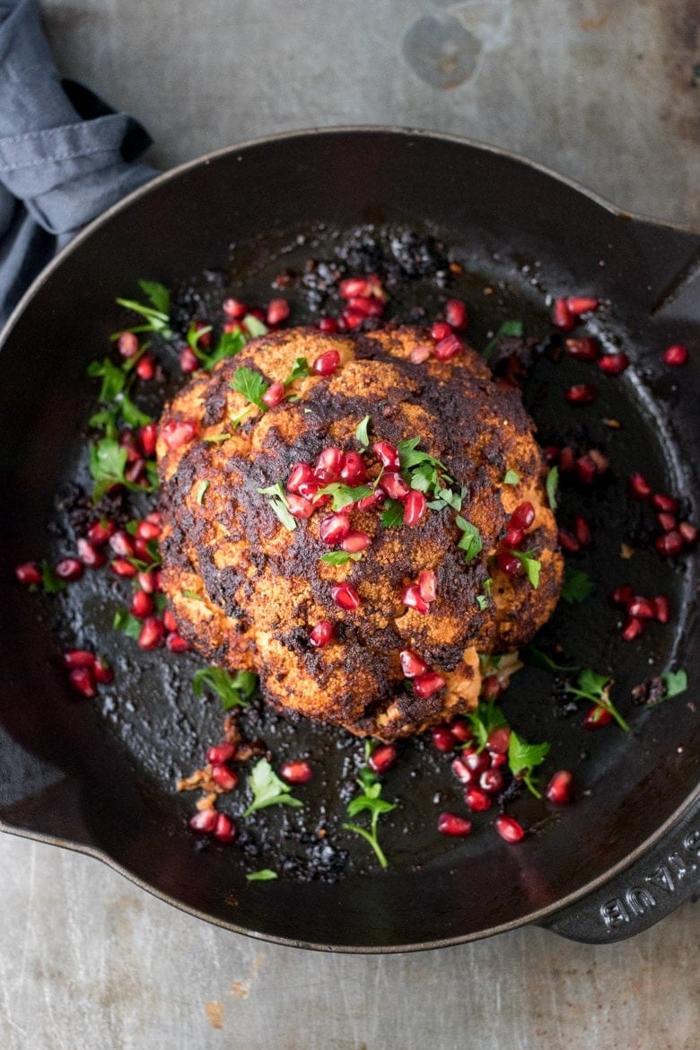 Whole cauliflower roasted in a pan garnished with pomegranate seeds. 