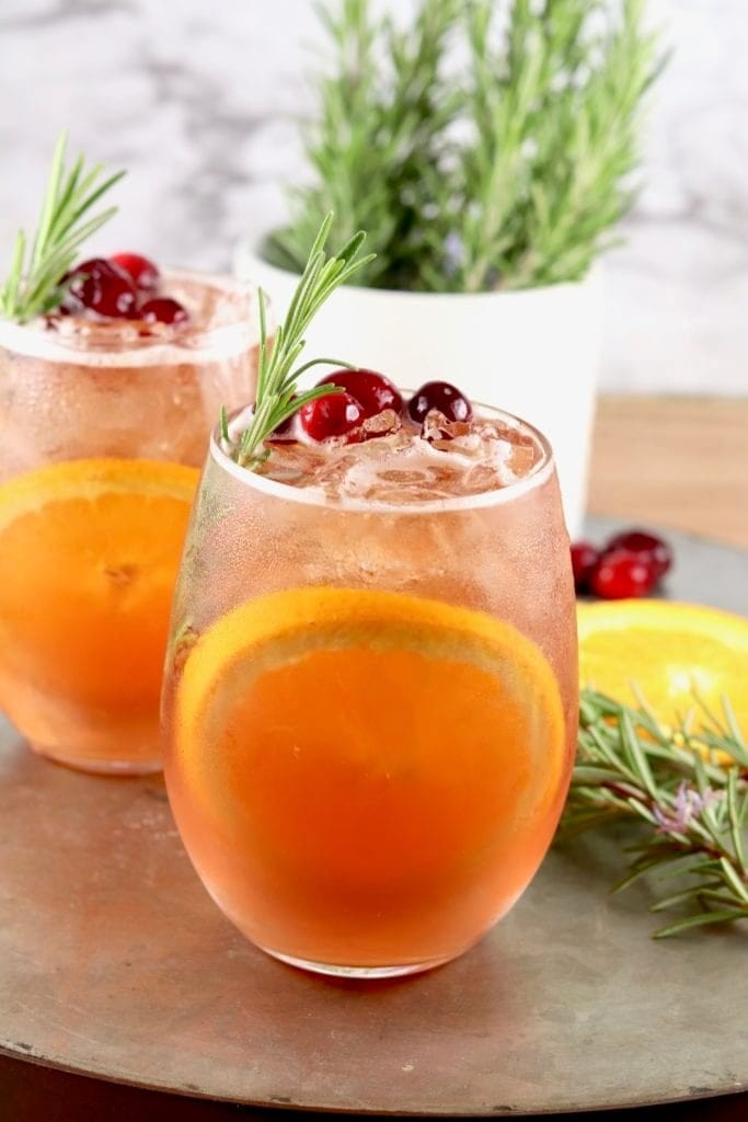 Two glasses of orange punch garnished with rosemary and orange slices.
