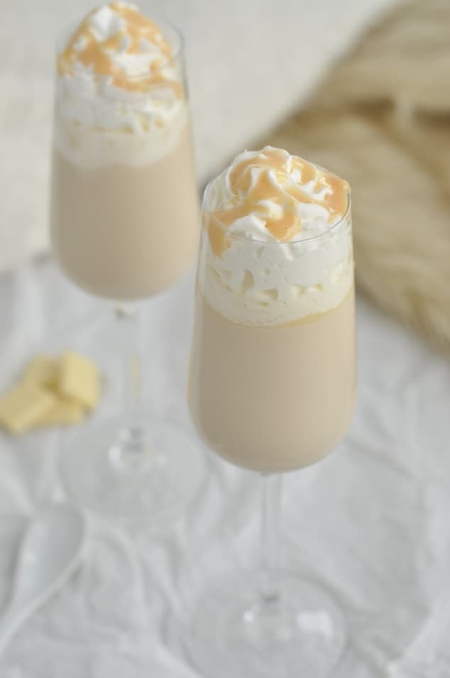 Two glasses of creamy cocktail topped with whipped cream and chocolate drizzle.