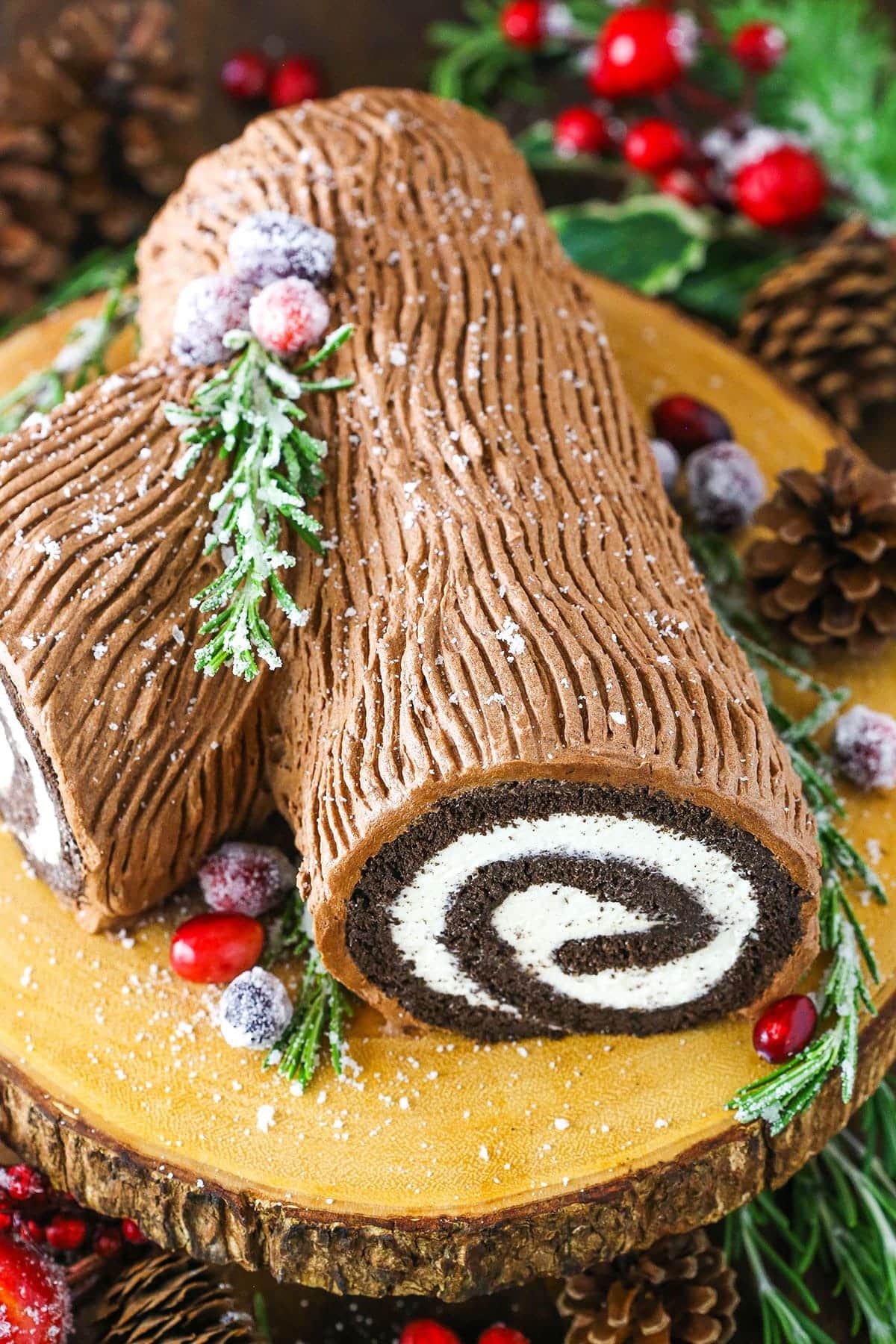 Log inspired chocolate Swiss roll cake decorated on top of a wooden chopping board. 