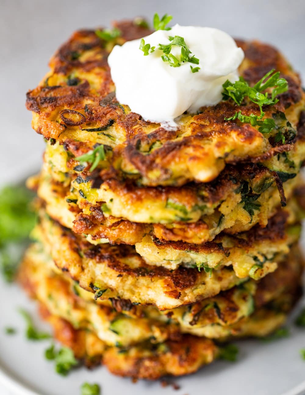 Stack of zucchini fritters with sour cream on top.