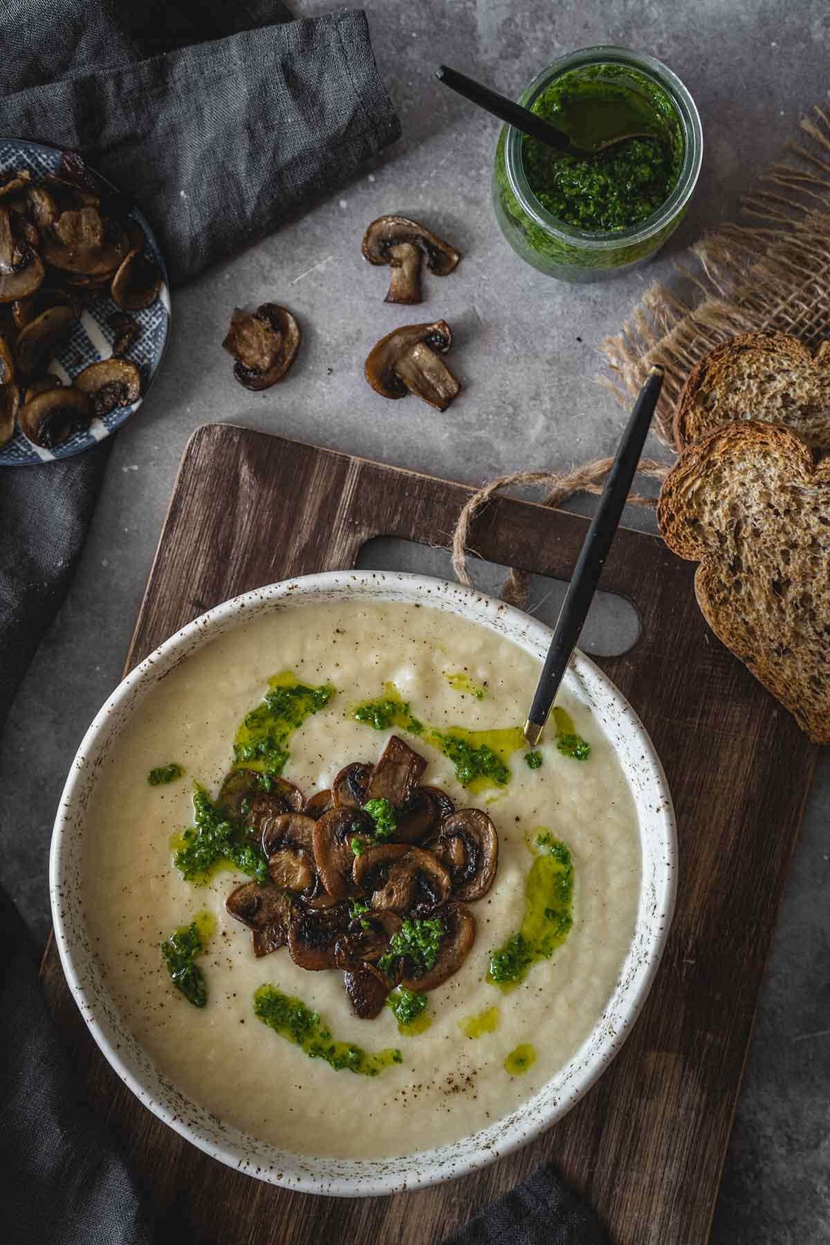 Creamy celery root soup with mushrooms and pesto in a bowl with a spoon- top view