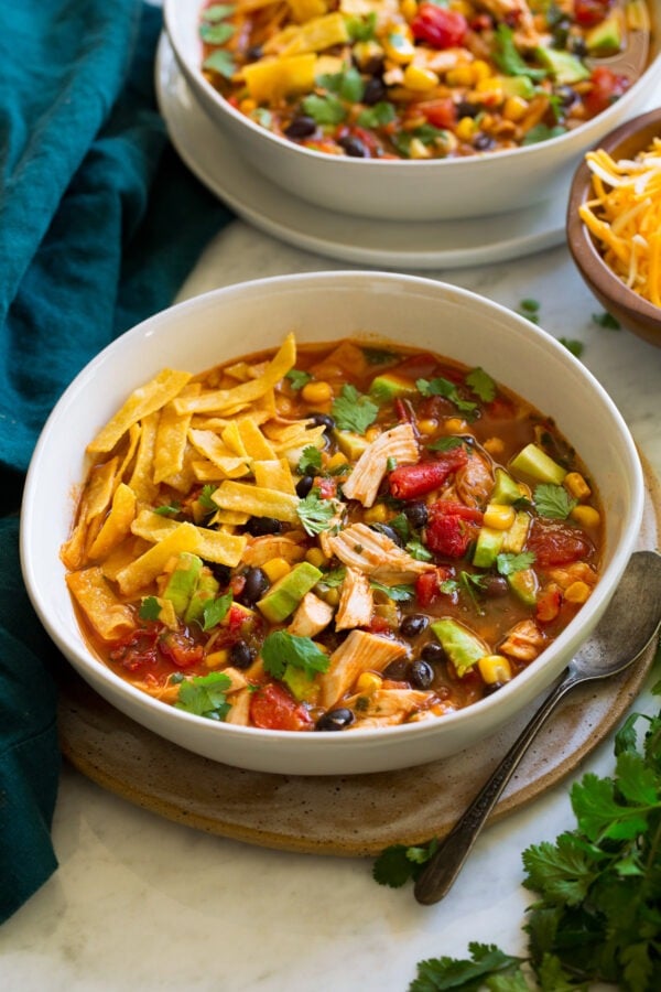 Chicken tortilla soup with chicken, avocado, beans, tortilla strips, cilantro, and tomatoes in a bowl