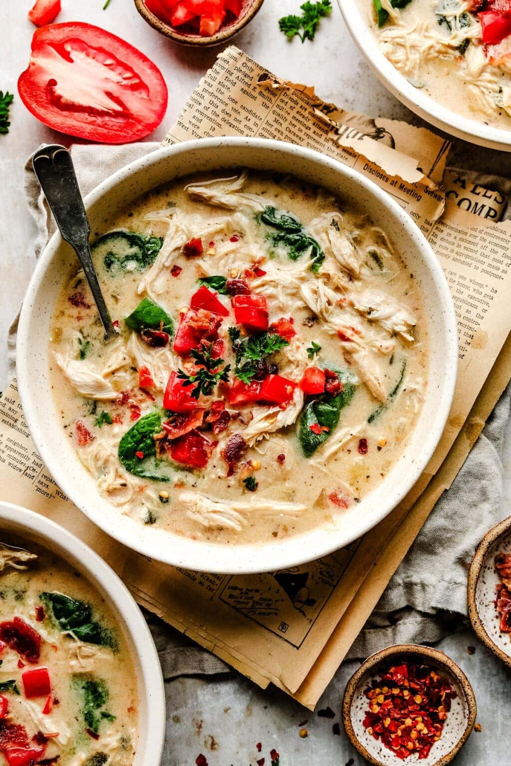 Creamy Italian chicken soup with tomatoes and spinach in a bowl with a spoon- close up top view with old newspapers in the backdrop