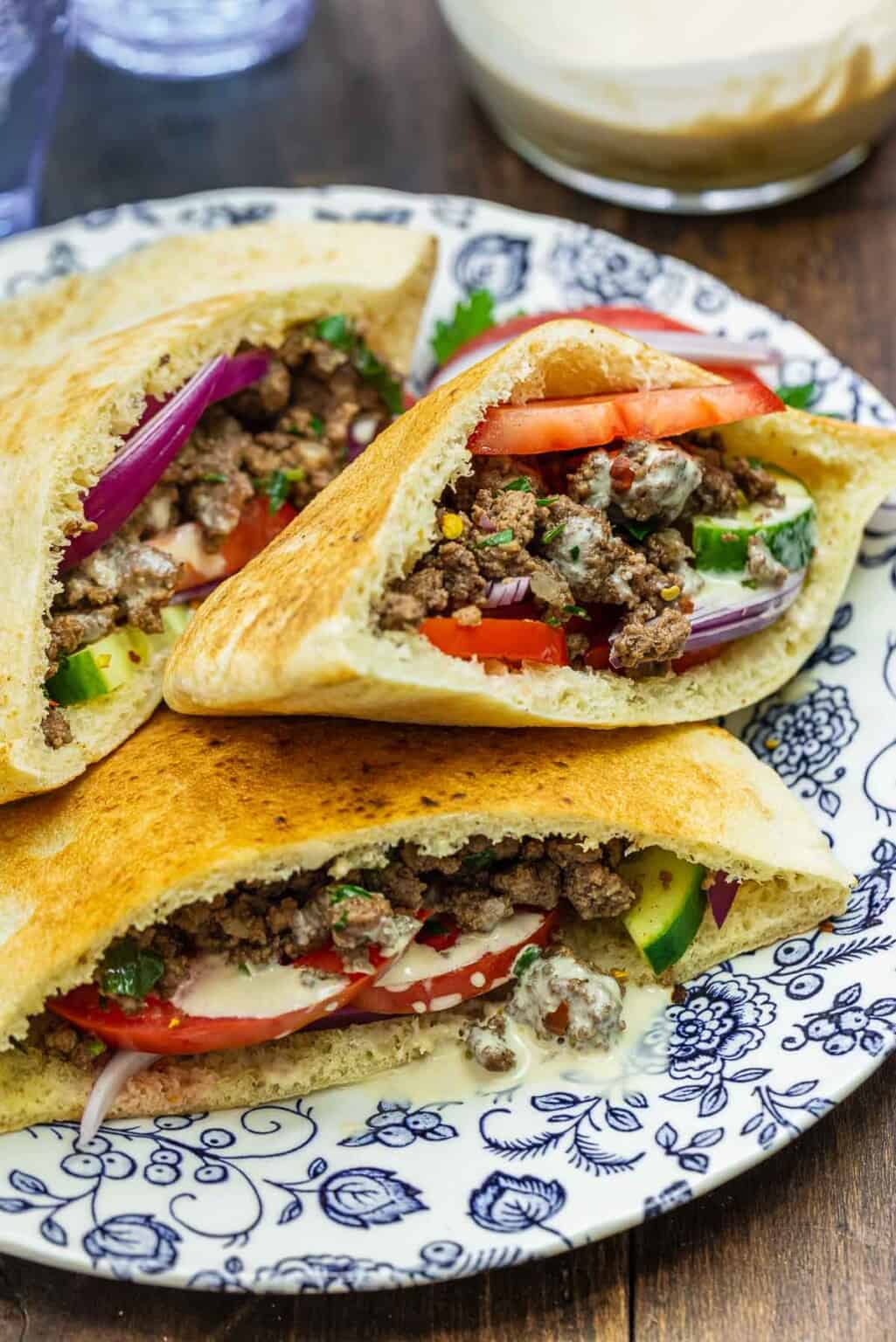 Delicious Ground Beef Pita Sandwich with Seasoned Ground Beef, Cucumbers, Red Onions, tomatoes, and Tzatziki Yogurt Sauce on Blue Floral and White Plates