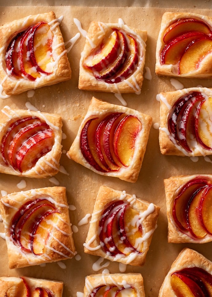 Pastry tarts topped with sliced peaches drizzled with sugar syrup. 
