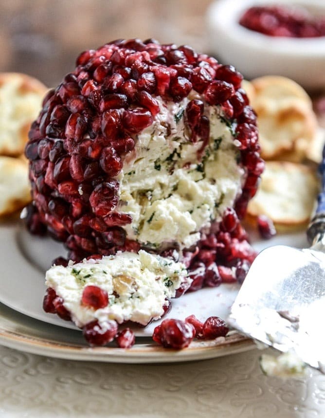 Pomegranate arils covered cheese ball sliced served on a plate.