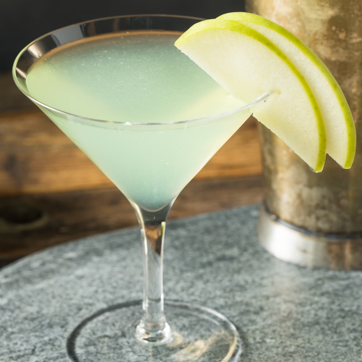 Appletini cocktail in a martini glass garnished with two slices of green apples.