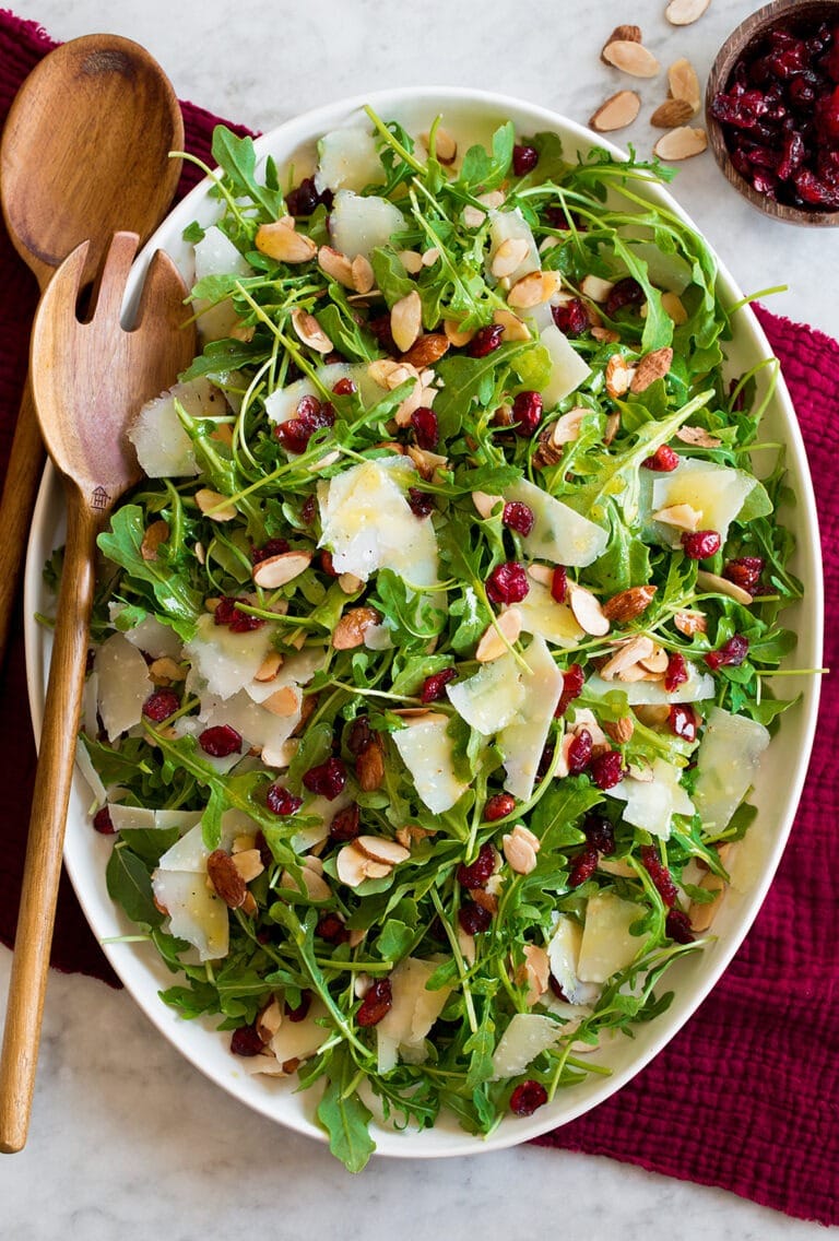 Arugula salad on an oval dish with peppery arugula, almonds, and cranberries.