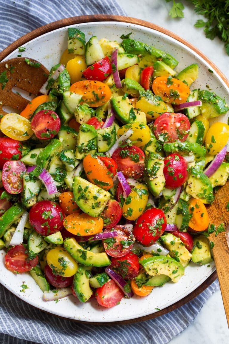 Avocado salad on a plate with  avocados, tomatoes, cucumbers, and onions.
