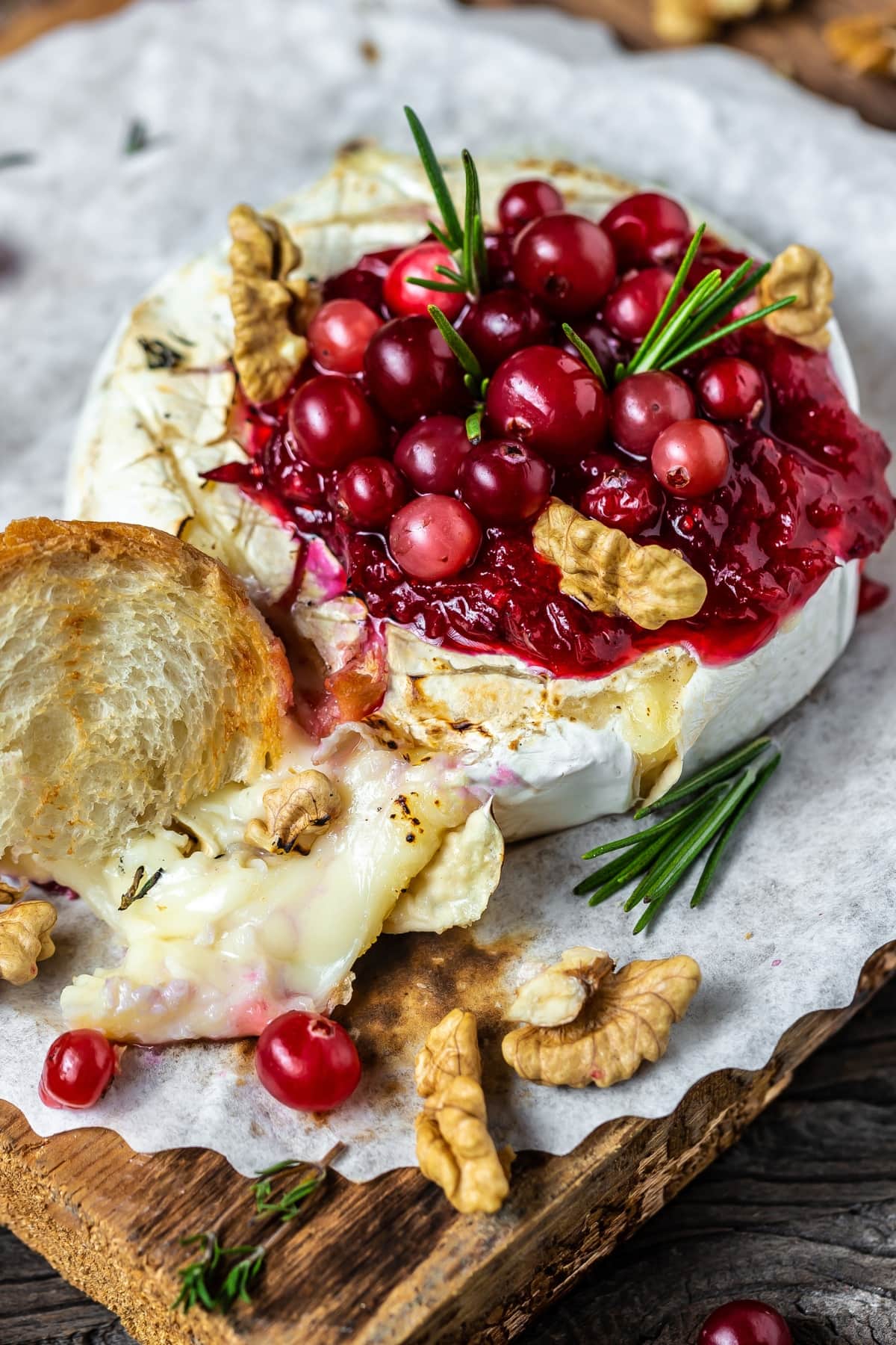 Baked brie with walnuts, cranberries and sauce on a wooden baord