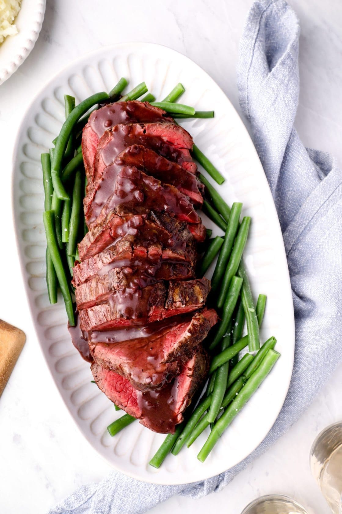 Sliced beef tenderloin drizzled with red wine sauce with green beans on side.