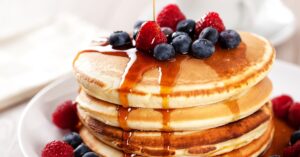 Stack of fluffy pancakes topped with berries drizzled with maple syrup.