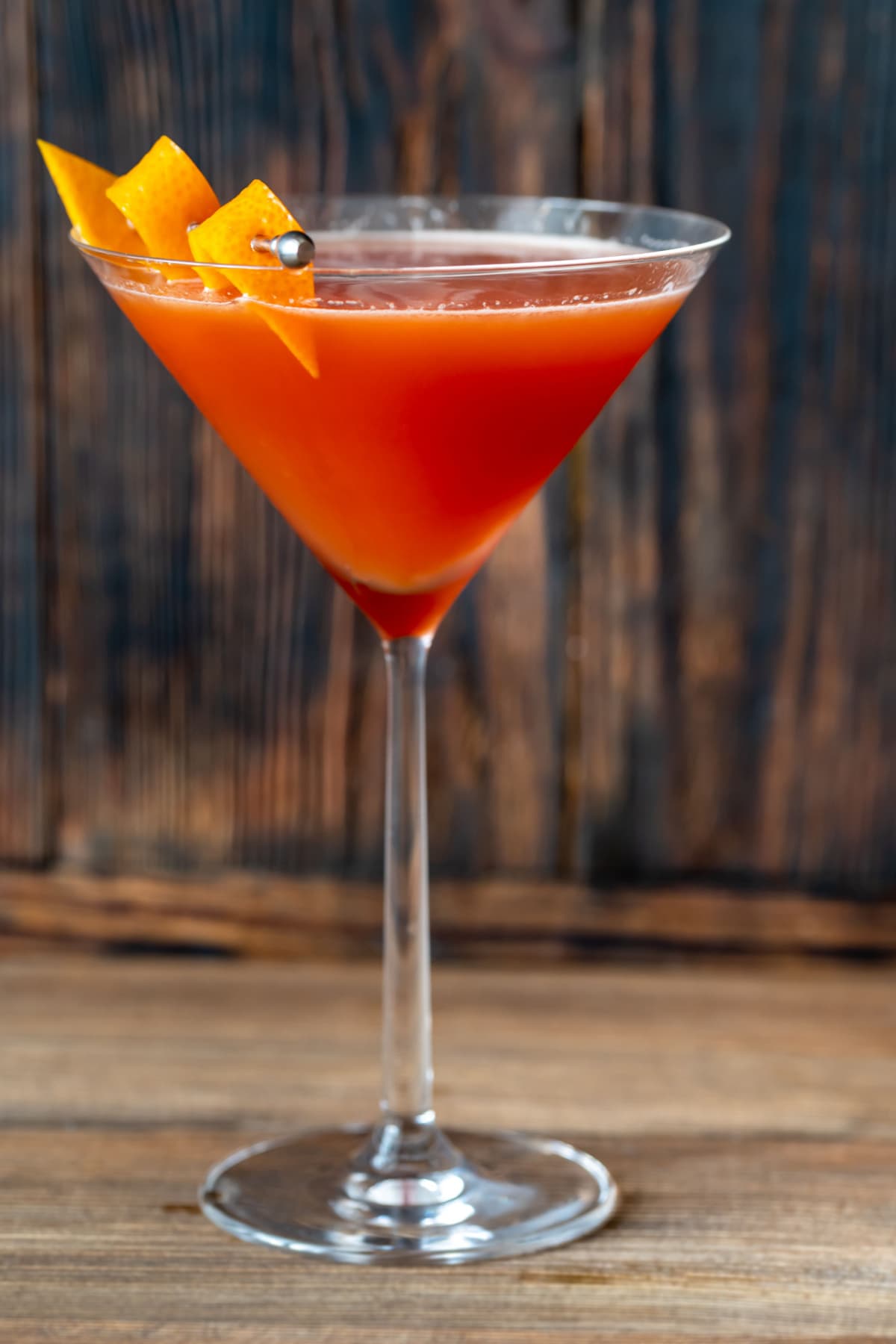 Orange red blood and sand cocktail served on a Martini glass garnished with an orange peel. 