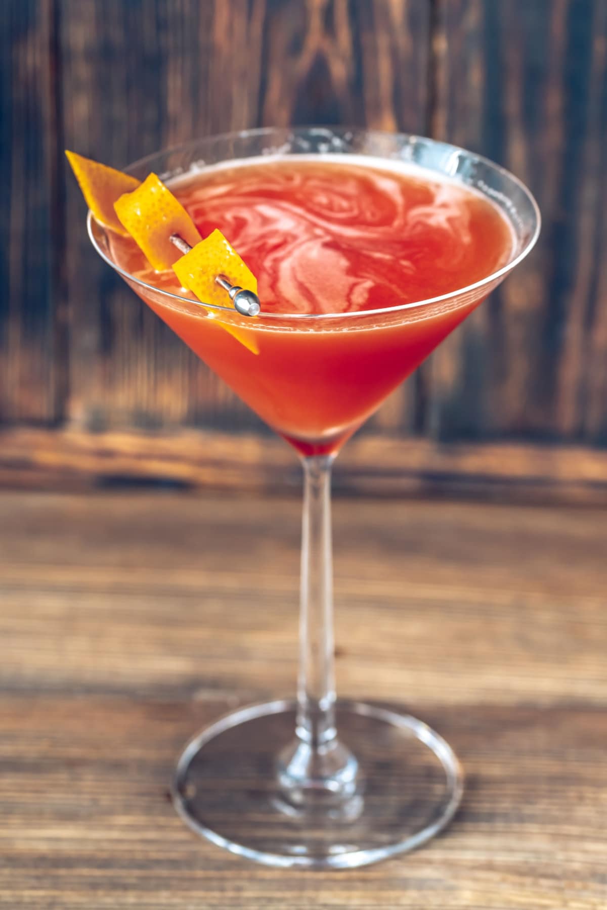 A serving of blood and sand cocktail on a martini glass garnished with lemon peel.
