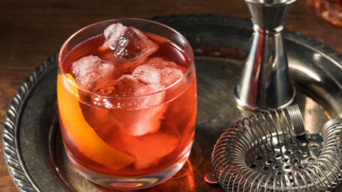 Boulevardier cocktail, mixer and strainer on a steel tray.