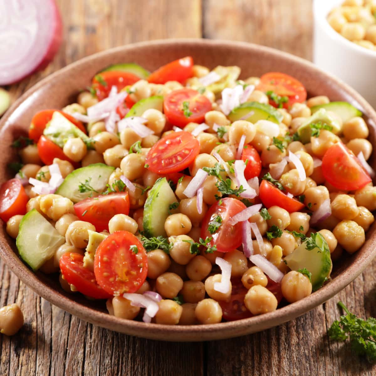Bowl of chickpea salad with  chickpeas, juicy tomatoes, crunchy cucumbers, creamy avocado garnished with chopped parsley leaves.