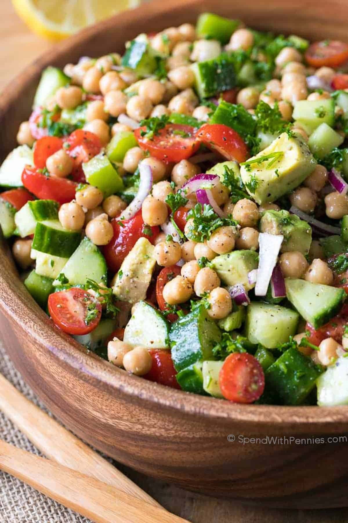 Wooden bowl with chickpea salad made with mix garbanzo beans, cucumber, tomatoes and dressing.
