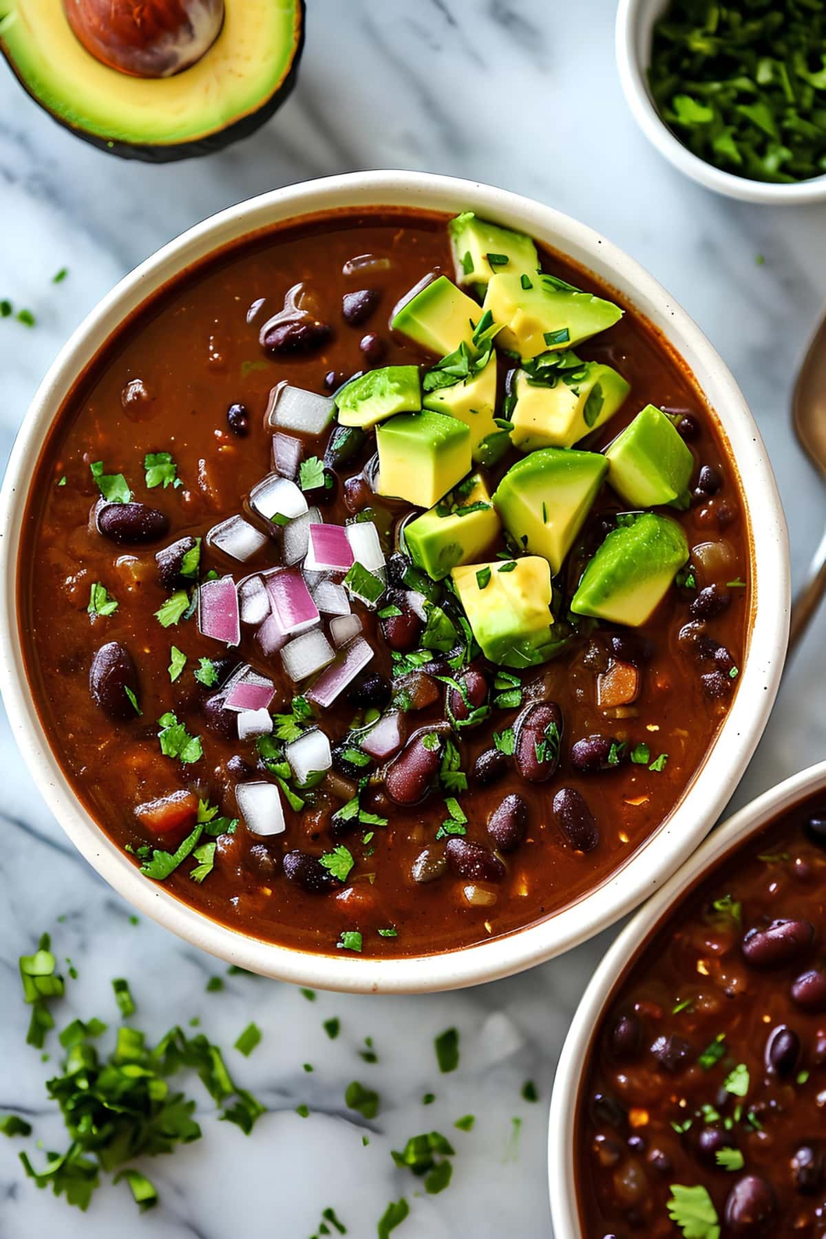 Chipotle black bean soup with chopped onions and avocados in a white bowl