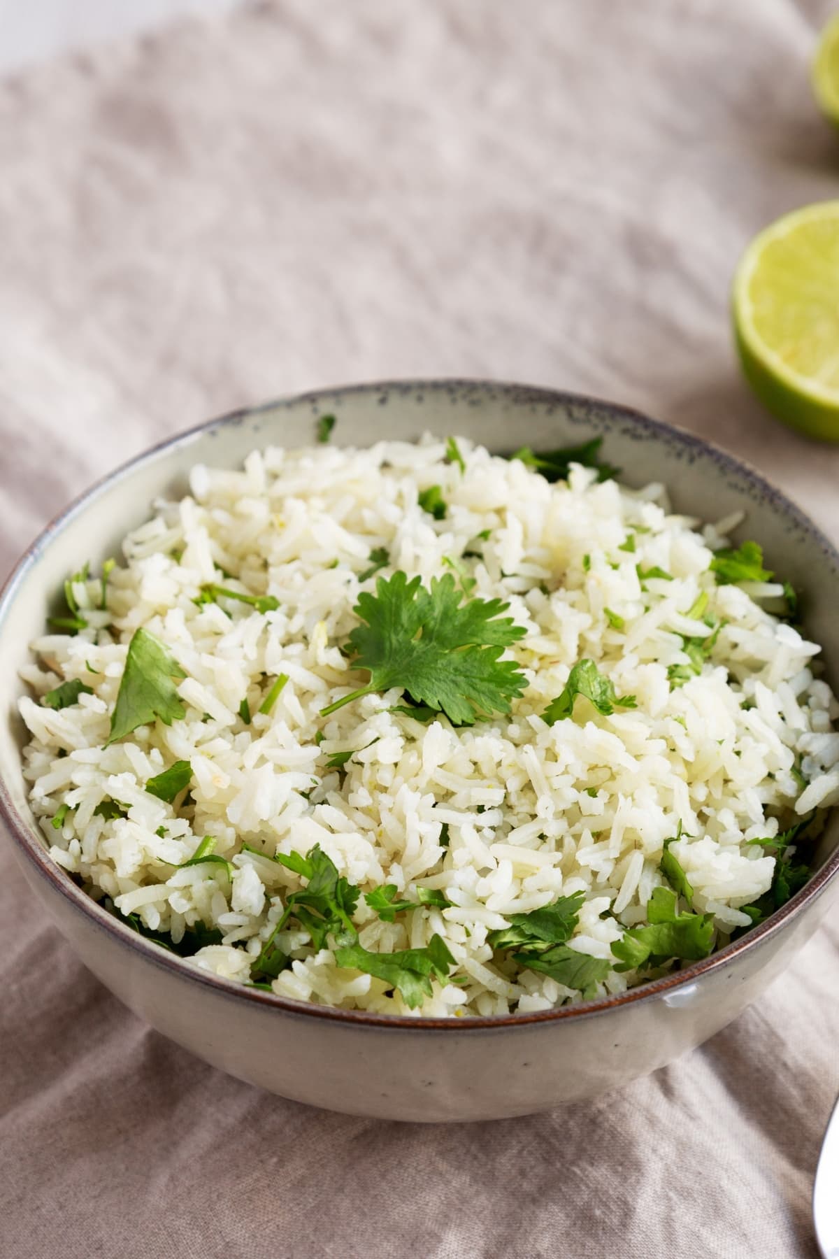 A bowl of cooked rice with cilantro and slice lime beside.