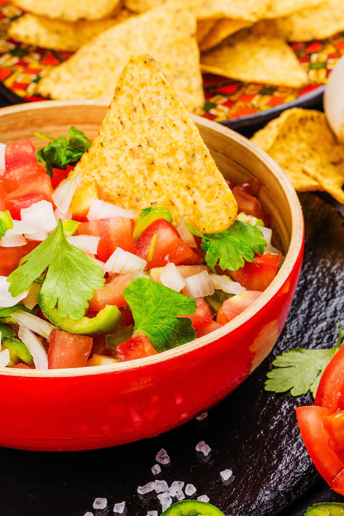 Pico de gallo with chopped tomatoes, onions, cilantro, and jalapenos served on a red bowl with nachos.