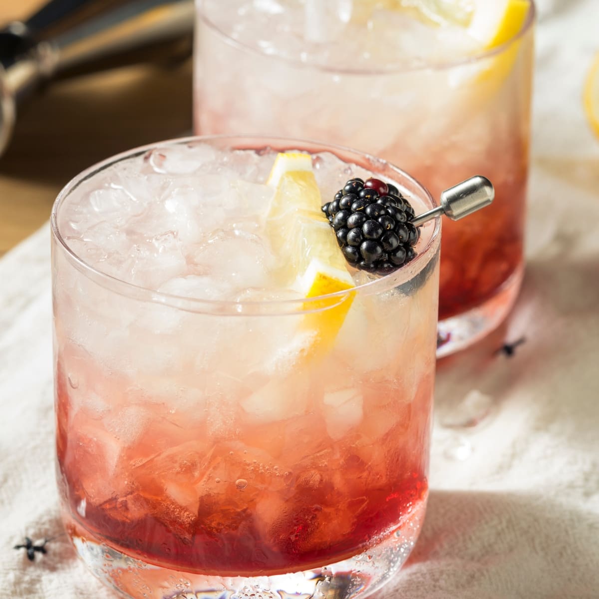Bramble cocktail in a glass with crushed ice with blackberries and lemon slice garnish. 