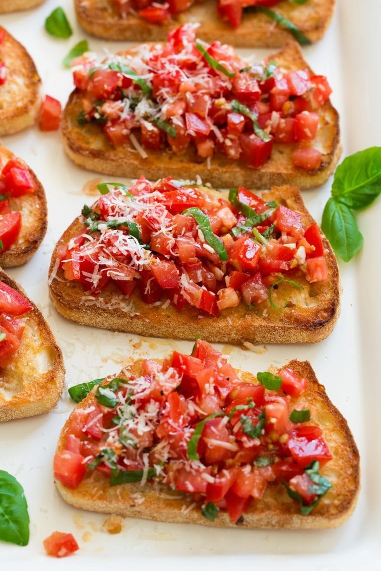 Toasted crostini topped with chopped tomato salsa garnished with parmesan cheese and chopped leaves.