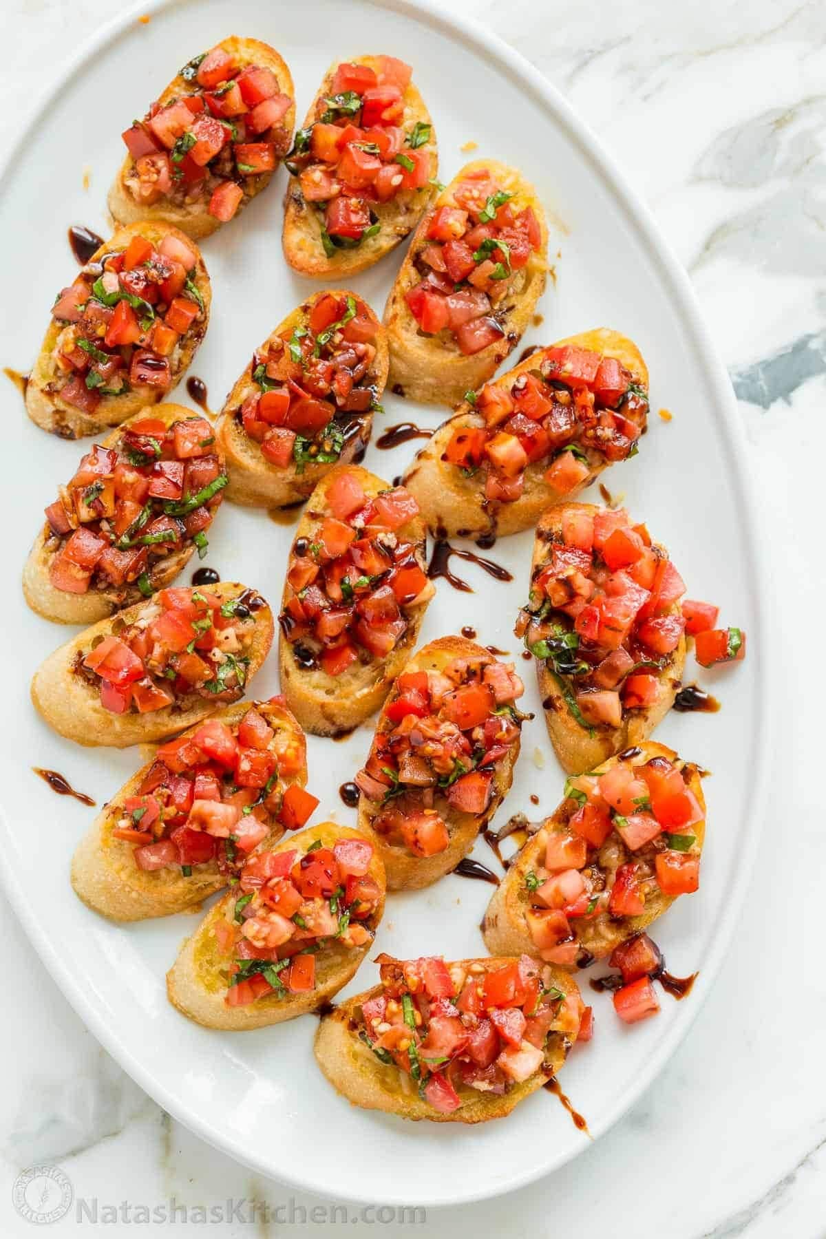 Sliced crostini topped with tomato and herbs drizzled with balsamic vinegar