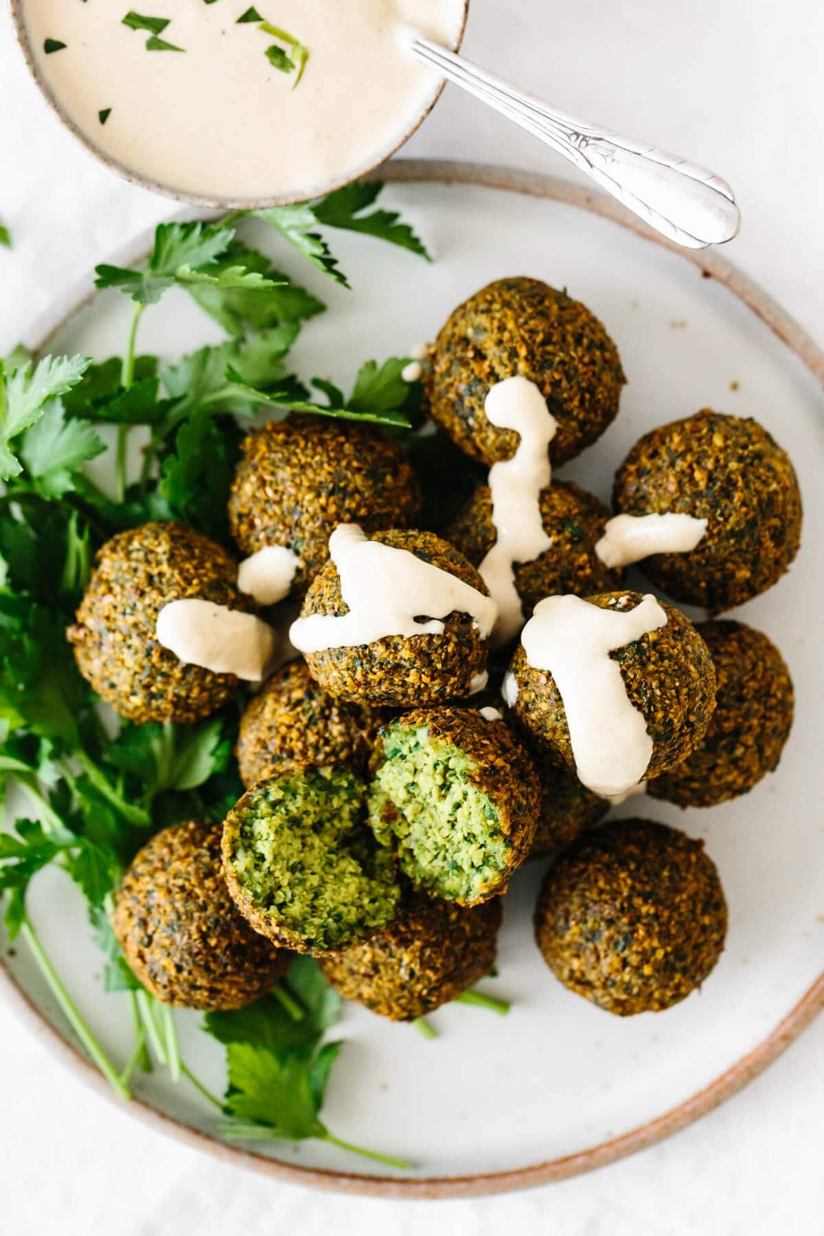 Bunch of falafel drizzled with white sauce garnished with fresh parsley leaves. 