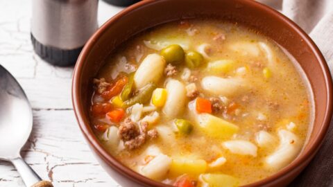 Busy day soup on a brown bowl made with elbow macaroni, green peas, carrots and broth.